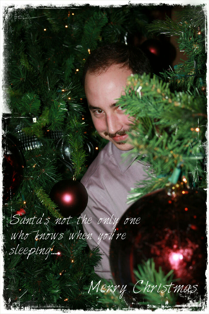 A funny Christmas card showing a man peeking through tree branches with festive ornaments.