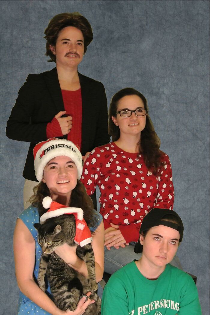 Group posing humorously for a funny Christmas card, one holding a cat in a Santa hat.
