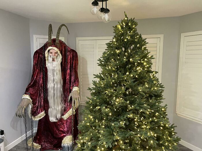 Dark-robed, horned figure surprising next to a Christmas tree, showcasing humorous holiday decoration creativity.