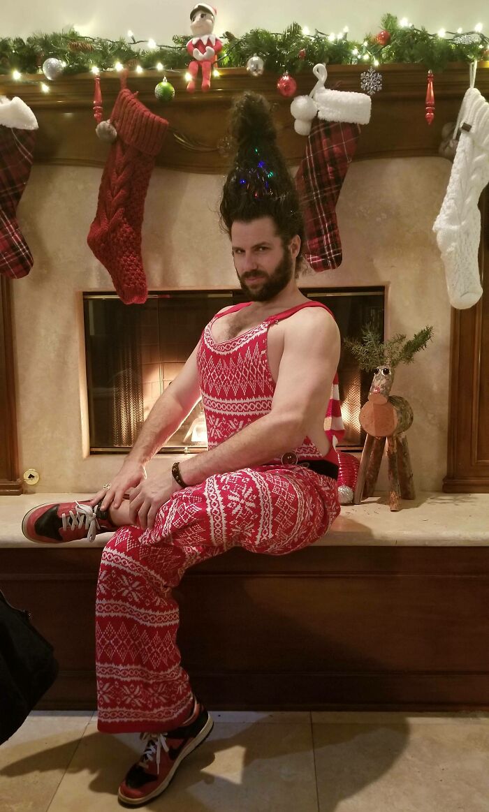 Man in festive red Christmas attire posing humorously by a decorated fireplace, capturing the spirit of funny Christmas cards.