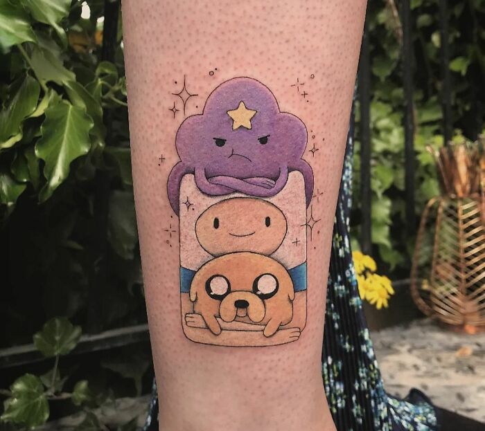 Cartoon tattoo of animated show characters on a person's leg, featuring colorful designs and details.
