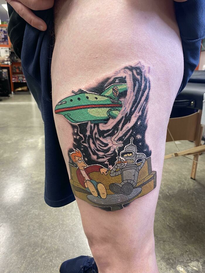 Cartoon tattoo featuring spaceship, robot, and character, evoking childhood favorites, on a person's leg.