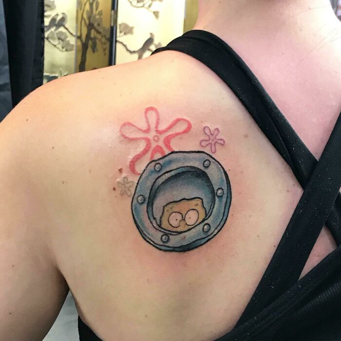 Tattoo of a cartoon character in a porthole on a person's shoulder, inspired by childhood favorites.
