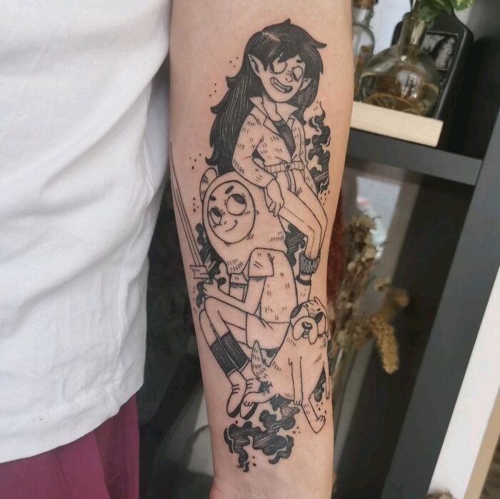 Cartoon tattoo on forearm featuring nostalgic animated characters in black ink.