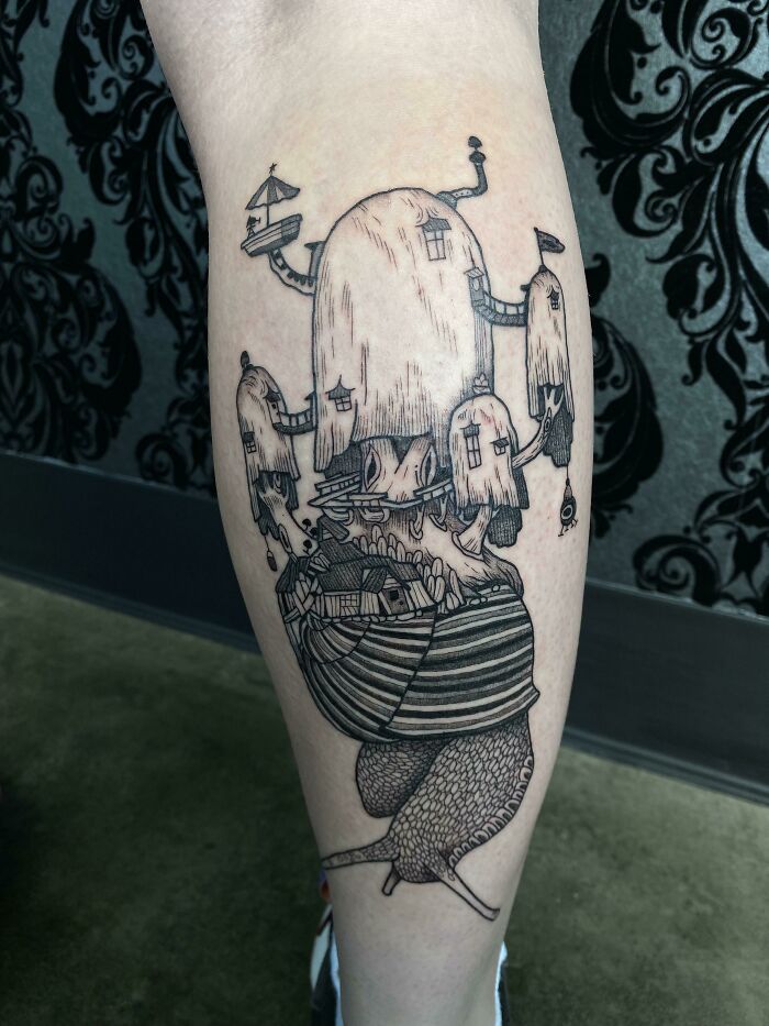 Cartoon tattoo featuring a snail with whimsical houses on its shell, showcasing creative ink design on a person's leg.