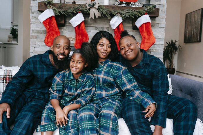 Family in matching pajamas smiling by a fireplace with stockings, celebrating New Year’s Eve together.