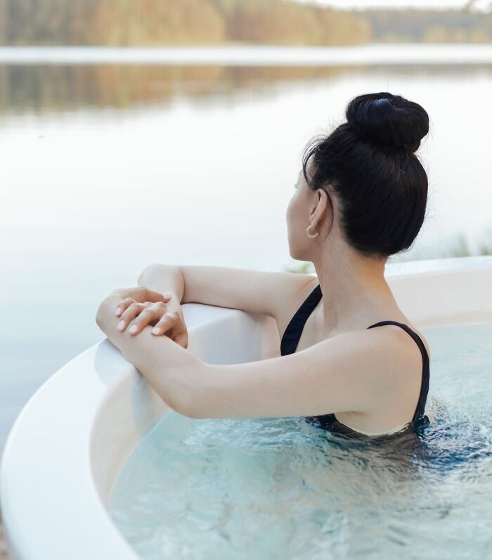 Person relaxing in a hot tub by a serene lake, enjoying a cool New Year's Eve moment.