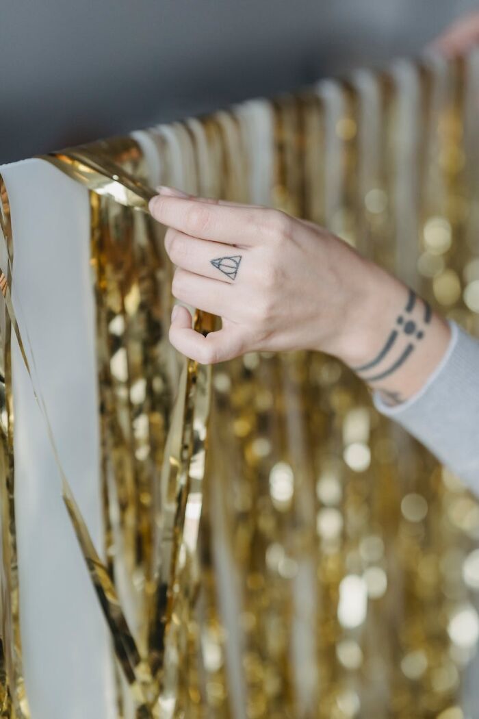 A hand arranging gold New Year’s Eve decorations with tattoos visible on wrist and fingers.