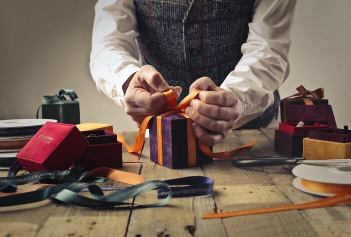 Hands wrapping a colorful New Year's Eve gift with ribbons on a rustic table.