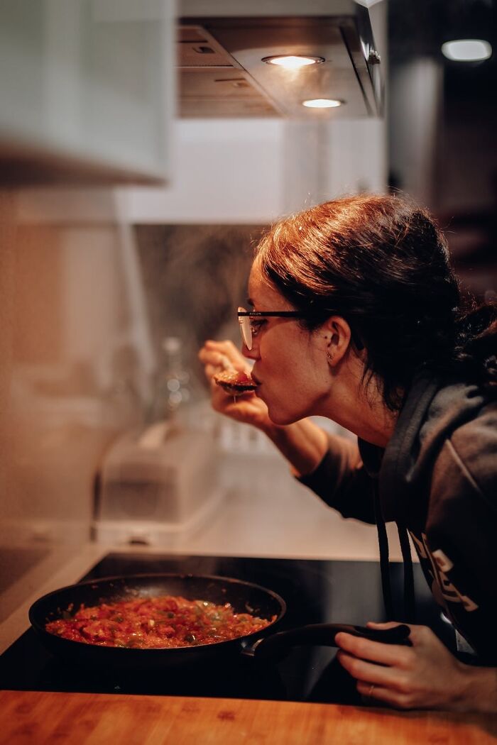 Woman tasting food from a pan on the stove, a cool thing to do on New Year’s Eve.