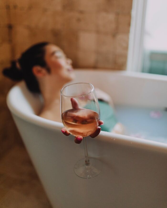 Person relaxing in a bathtub, holding a wine glass, enjoying a cool New Year’s Eve moment.