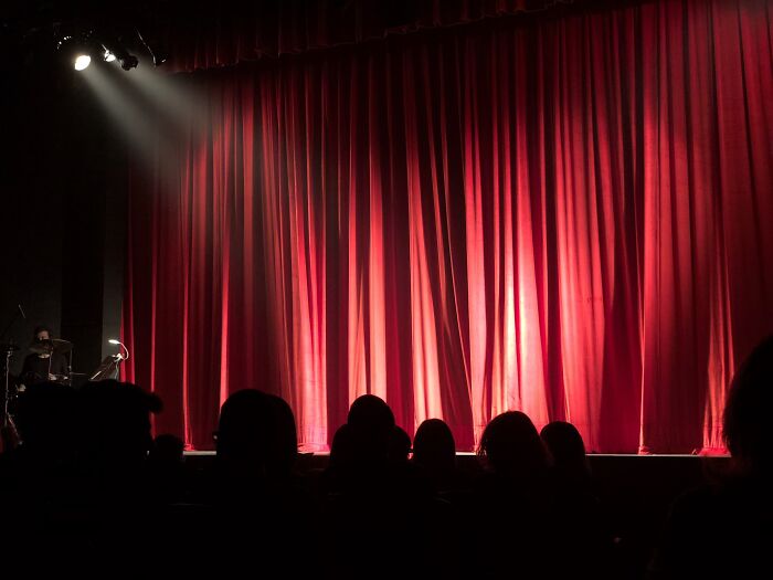 Red theater curtains on stage with audience silhouettes, illuminated by spotlight for cool New Year’s Eve performance.