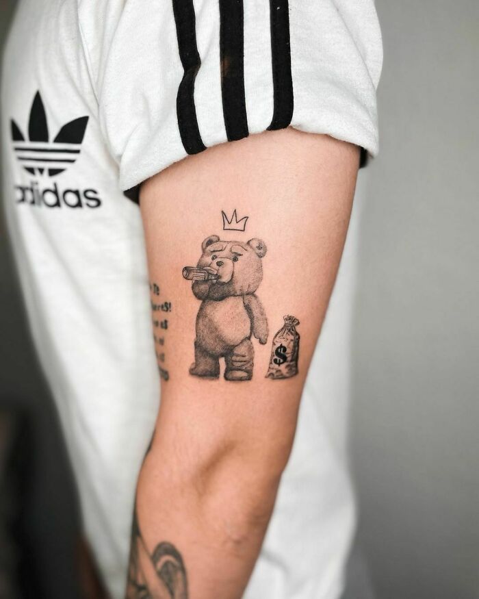 Cartoon tattoo of a bear with a crown and money bag on a person's arm, inspired by animated shows.