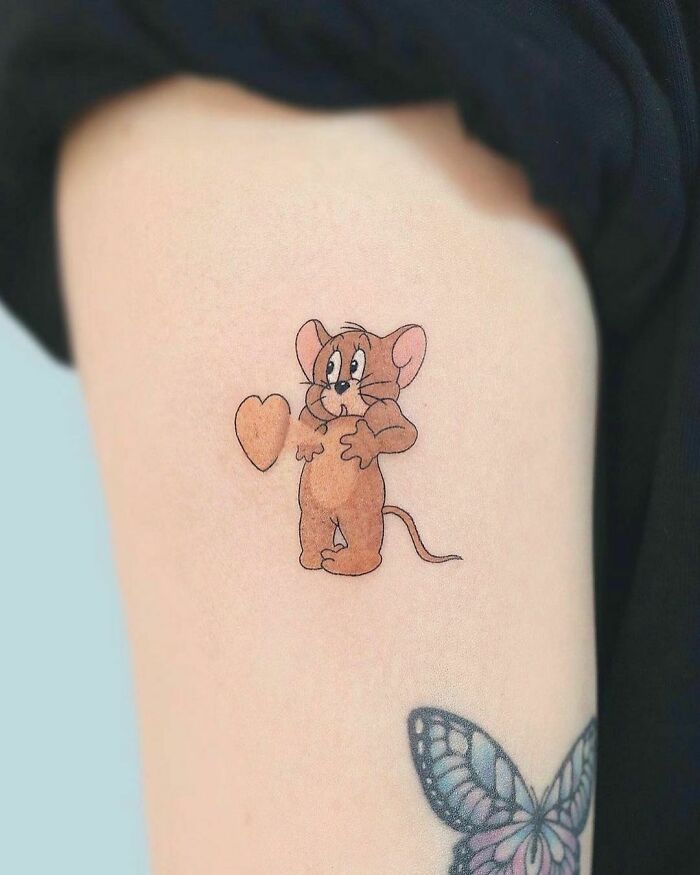 Cartoon tattoo of a mouse from an animated show with a heart symbol next to it, on an arm above a colorful butterfly.