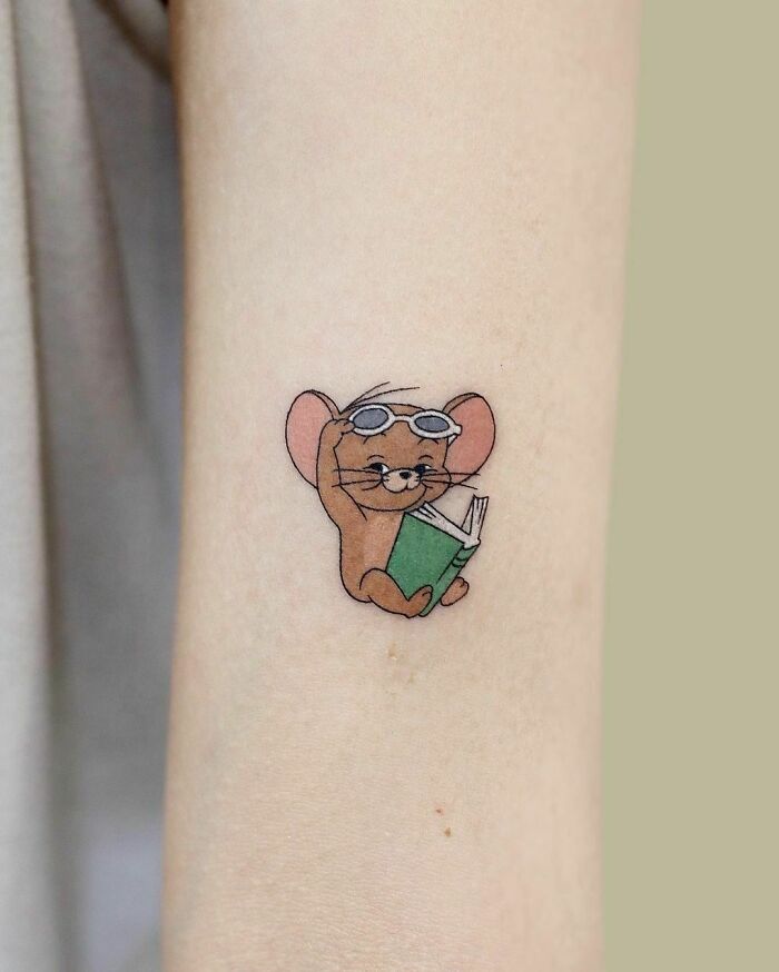 Cartoon tattoo of Jerry from "Tom and Jerry" reading a book, capturing a nostalgic vibe.