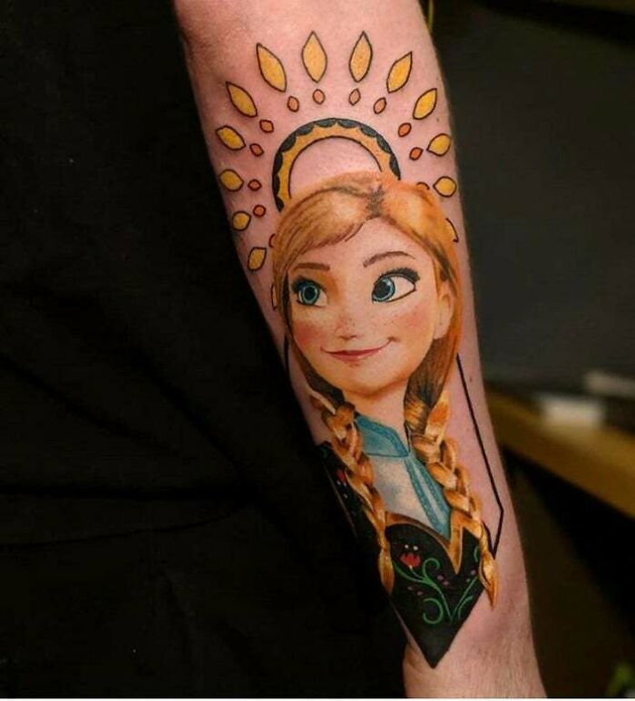 Cartoon tattoo on arm featuring a character Anna with braided hair and halo, showcasing vibrant colors and intricate details.