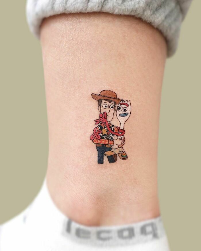 Cartoon tattoo featuring two animated characters holding each other on an ankle.