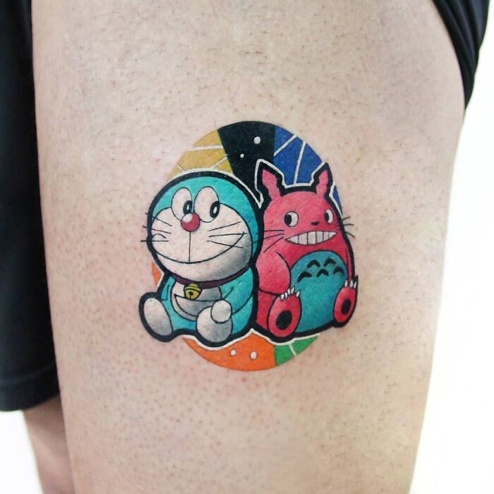 Cartoon tattoos featuring a blue robotic cat Doraemon and a smiling Totoro creature on a colorful circular patch.