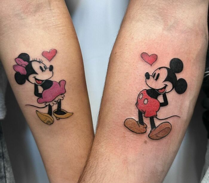 Cartoon tattoos of Mickey Mouse and Minnie on forearms, evoking nostalgia with heart accents.