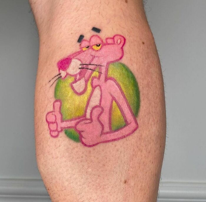 Cartoon tattoo of a pink panther with thumbs up on skin, evoking childhood favorites.