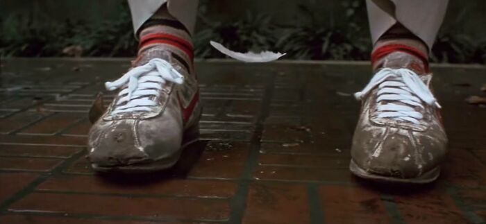 Worn white sneakers and striped socks on brick pavement with a floating feather, showcasing Easter eggs in popular films.