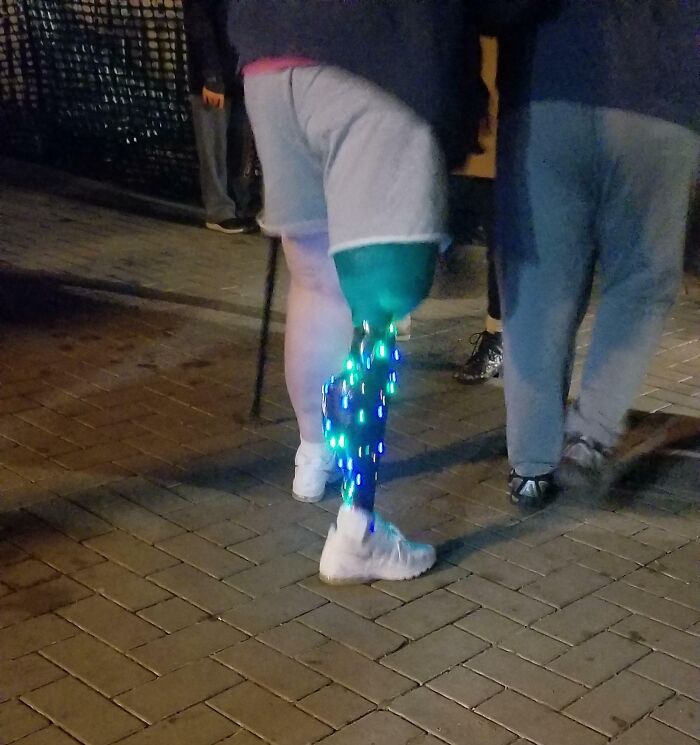 Person with a prosthetic leg adorned with Christmas lights, showcasing a sense of humor on a festive evening walk.