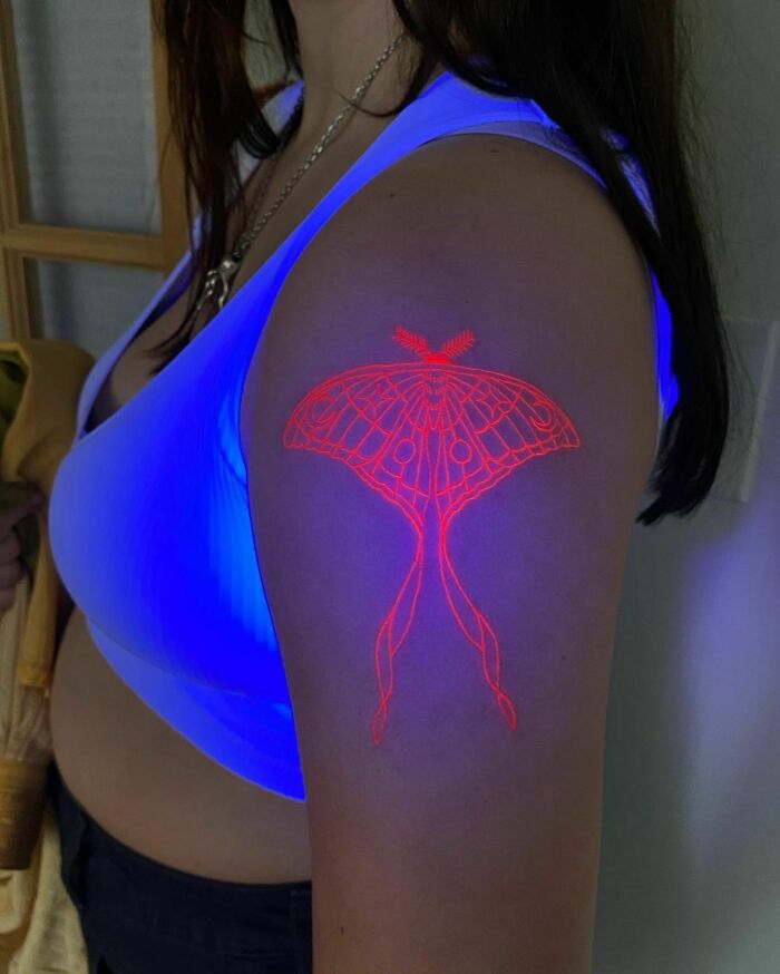 Ultraviolet trippy moth tattoo on a person's shoulder, glowing under blacklight.