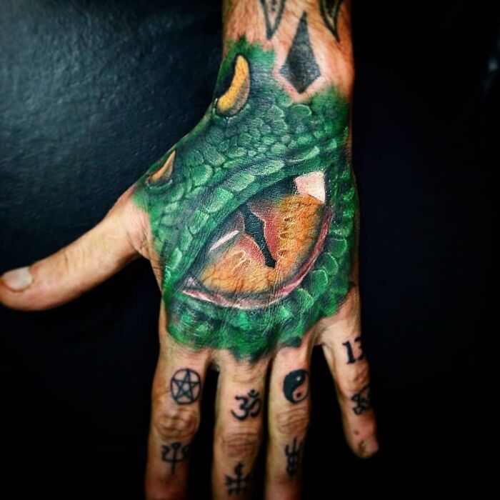 A vibrant trippy tattoo of a snake's eye on a hand, surrounded by various small symbols on the fingers.