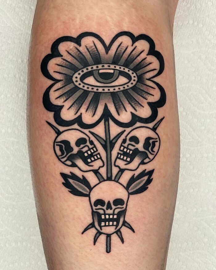 Trippy skulls and flower with eye tattoo on arm, featuring bold black ink design.