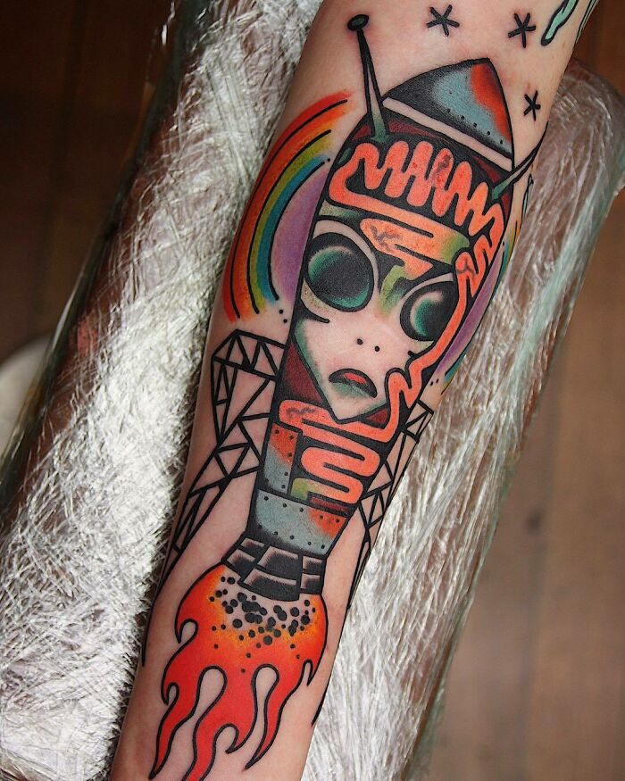 Trippy tattoo of an abstract rocket with geometric patterns and vibrant colors on forearm.