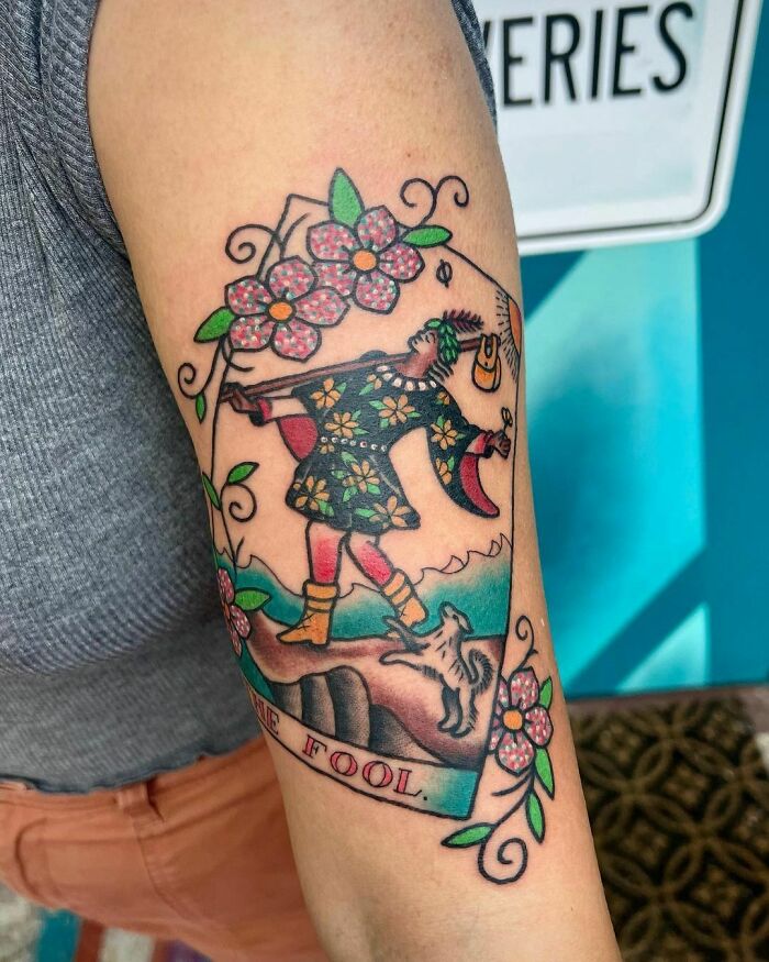 Trippy tattoo of a colorful, floral-patterned character walking with a dog, inspired by tarot imagery.