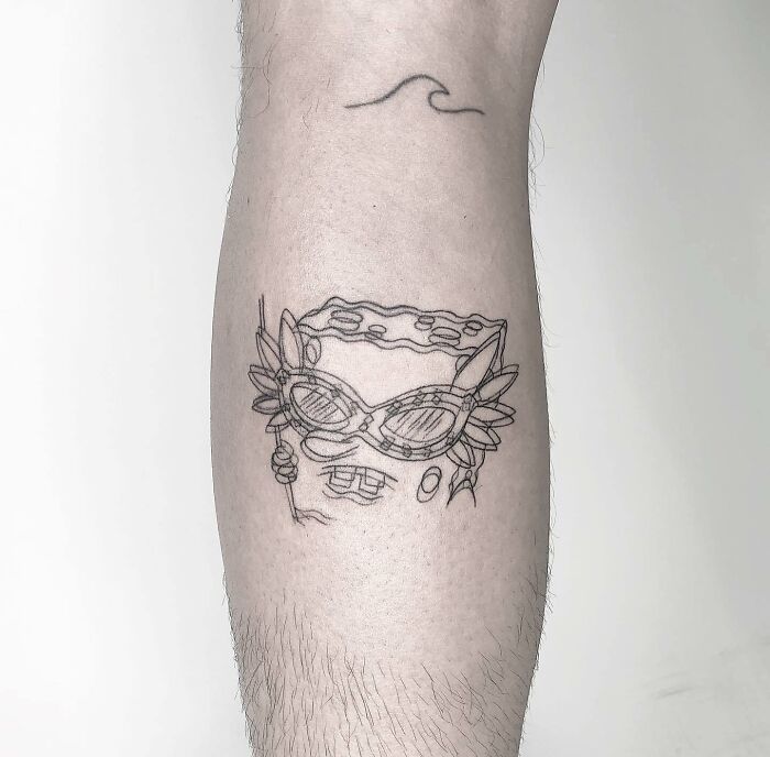 Trippy tattoo of a character with glasses and floral elements on a person's leg, featuring minimalist abstract lines.