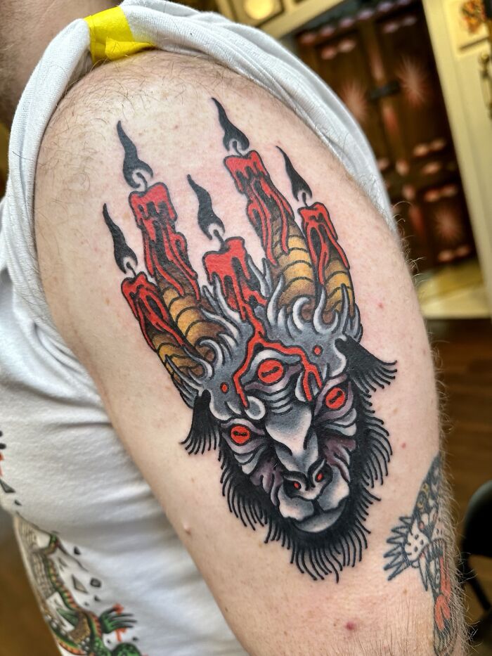 Trippy tattoo of mythical creature with red and yellow elements on arm.