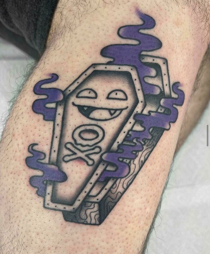 Trippy tattoo featuring a smiling coffin with purple smoke, blending geometric and cartoon elements on the skin.