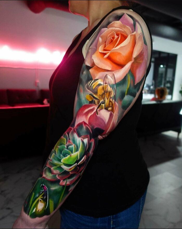 Colorful floral and insect-themed trippy tattoo sleeve on an arm, featuring a rose, bee, and succulent.