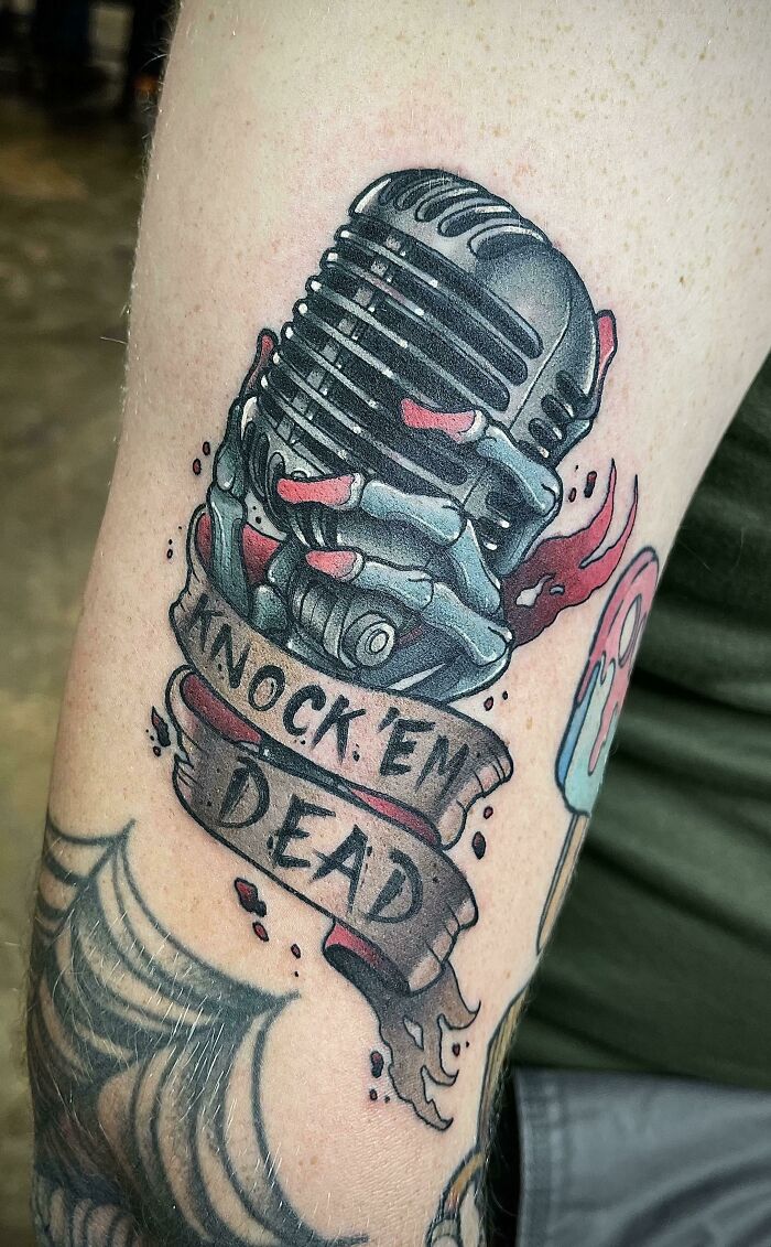 Trippy tattoo of a vintage microphone with a skeletal hand and a banner reading "Knock 'Em Dead."