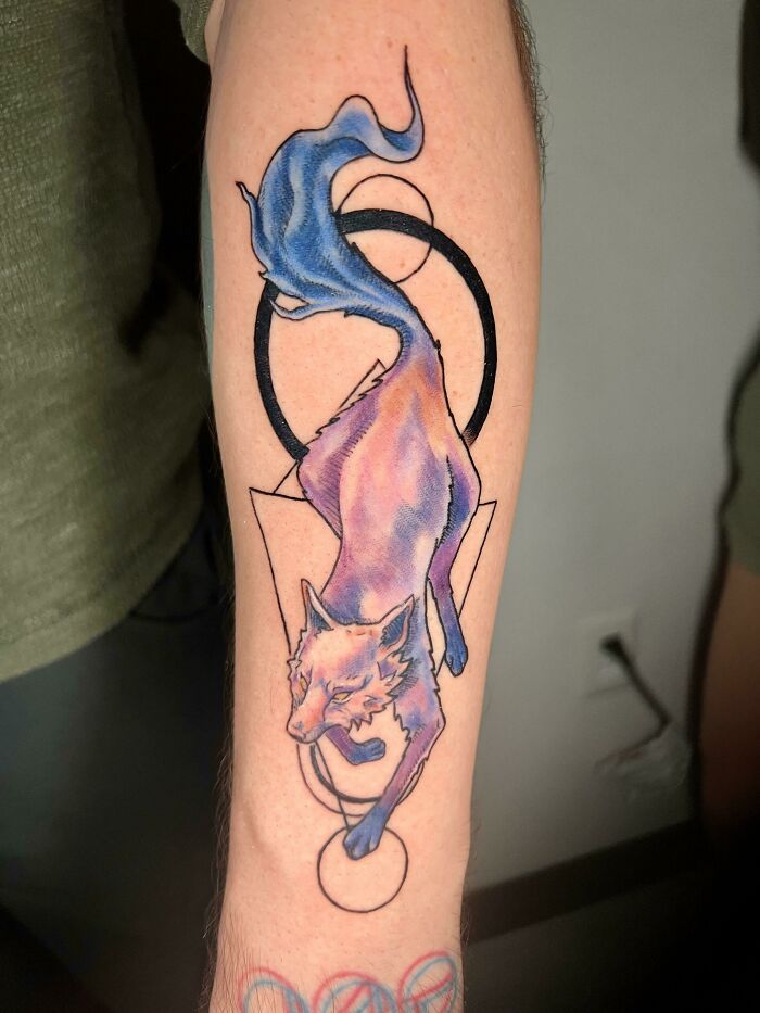 Psychedelic art tattoo of a colorful fox with geometric shapes on an arm.