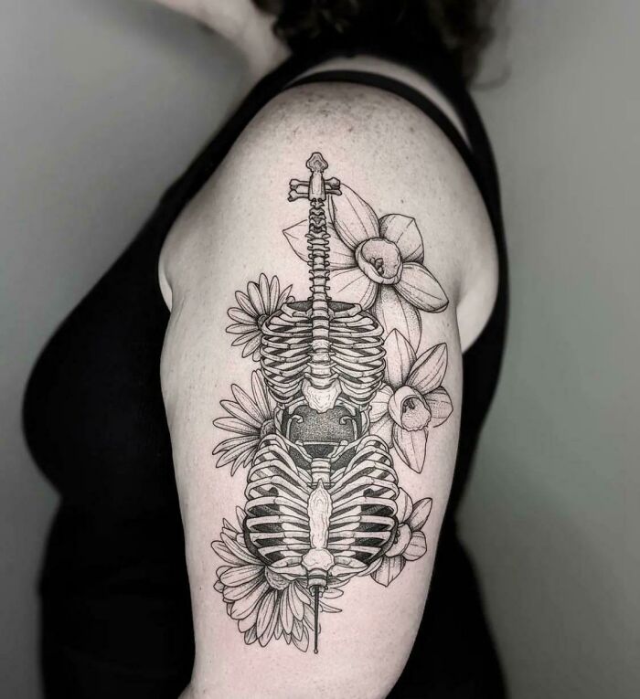 Trippy tattoo of a bone cello with daisies and daffodils on a shoulder.