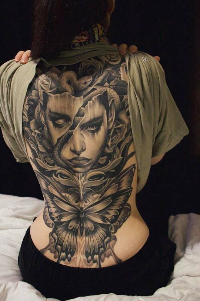 Back tattoo of a surreal face with a snake and butterfly, showcasing trippy tattoo design on a woman's back.