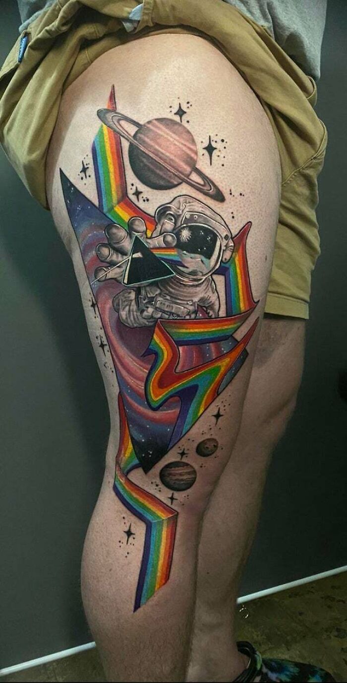 Astronaut tattoo with psychedelic art featuring rainbow and planets on a leg.