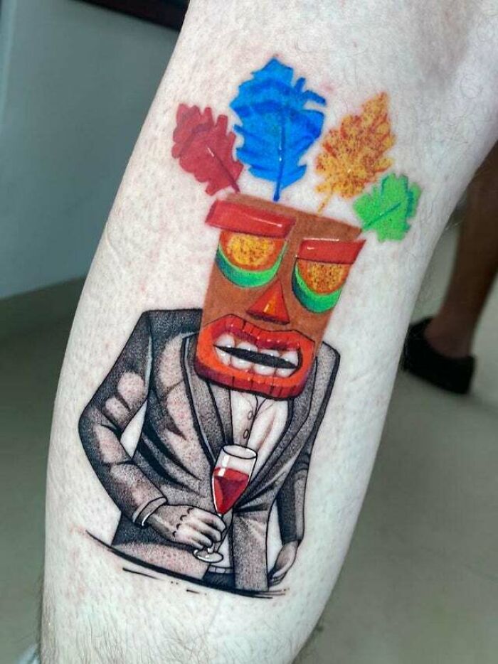 Colorful trippy tattoo of a tiki figure in a suit holding a glass of wine on forearm.