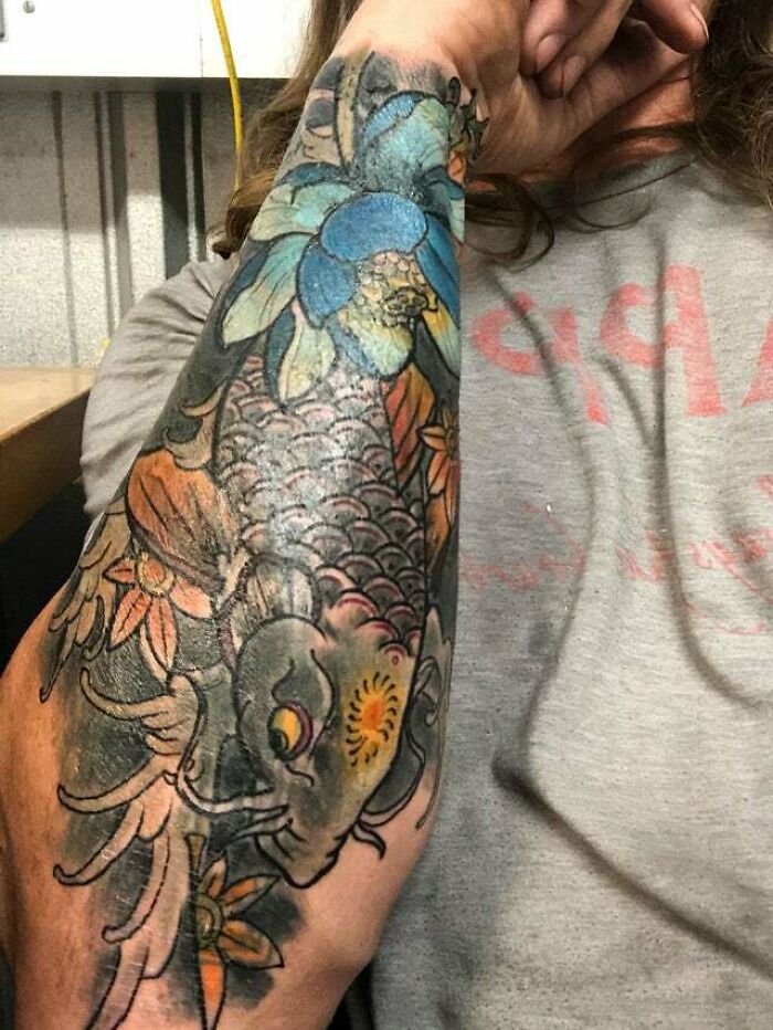 Arm tattoo with colorful koi fish and flowers, perfect for fans of psychedelic art.