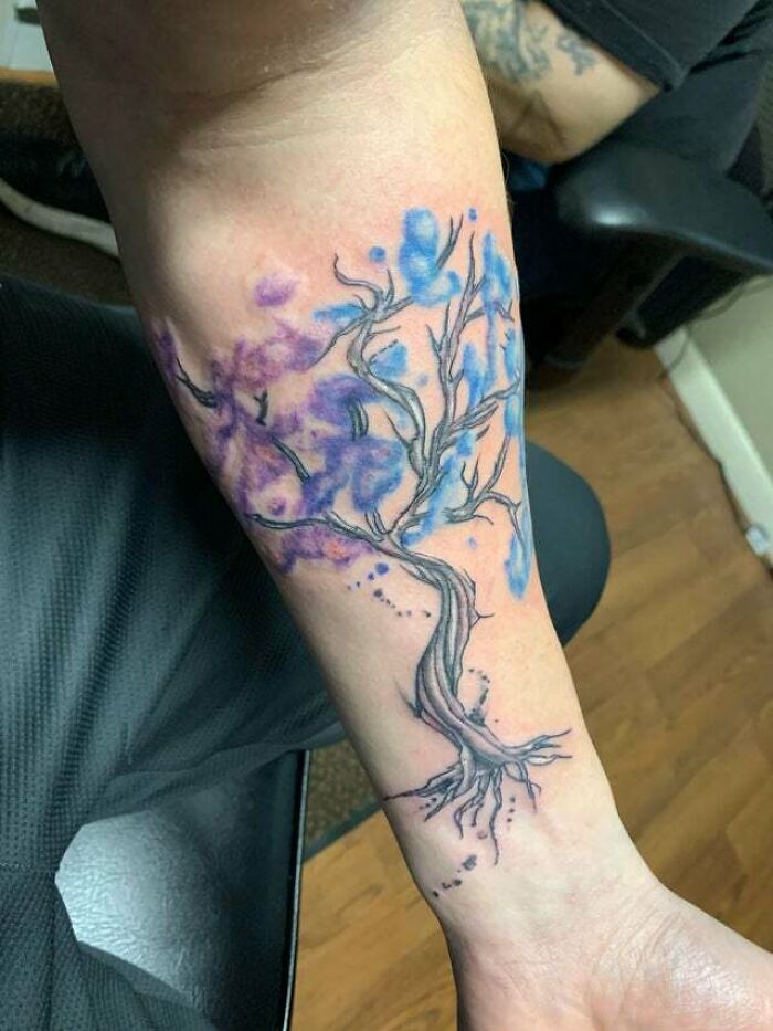 Trippy watercolor tree of life tattoo on a forearm with blue and purple hues.