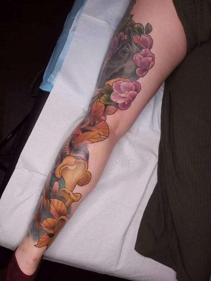 Colorful trippy tattoo on a leg featuring a horse, flowers, and mushrooms, showcasing vibrant artistry.