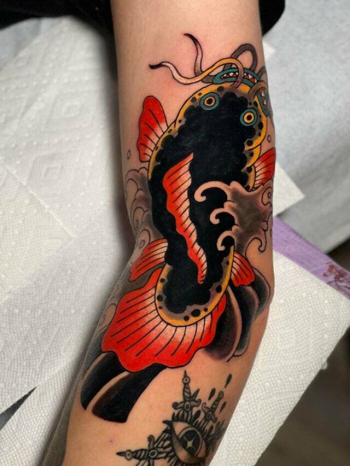 Colorful psychedelic tattoo of a koi fish on an arm, featuring bold reds and intricate black details.