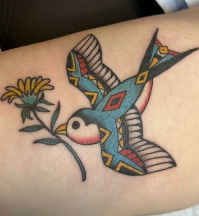 Trippy tattoo of a geometric bird with intricate patterns holding a flower in its beak.