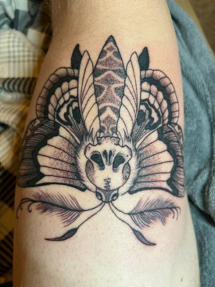 Trippy tattoo of a moth with a skull on an arm, showcasing intricate line work and shading.