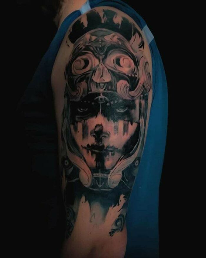 Trippy tattoo on an arm featuring a complex, abstract face design in black and gray ink.