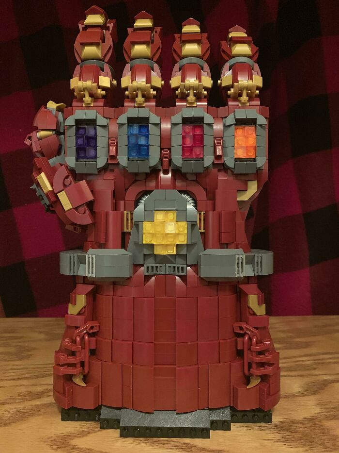 LEGO build of a detailed red gauntlet with colorful blocks, showcasing incredible LEGO art on a wooden surface.