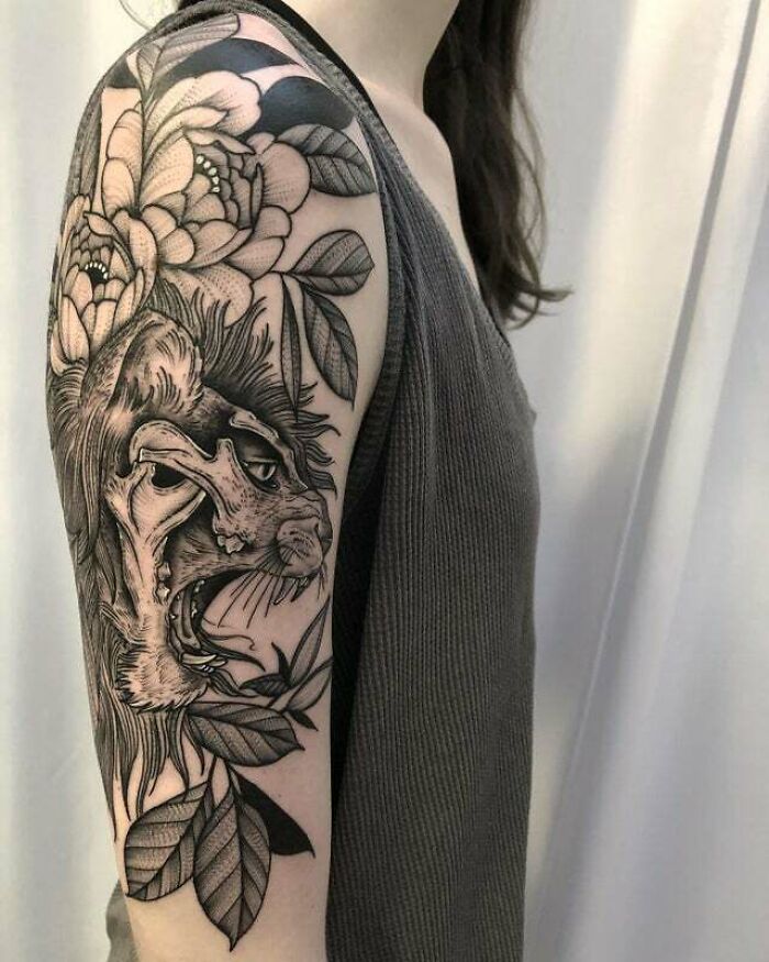 Arm with a trippy tattoo featuring a lion skull and flowers, blending elements of psychedelic art.